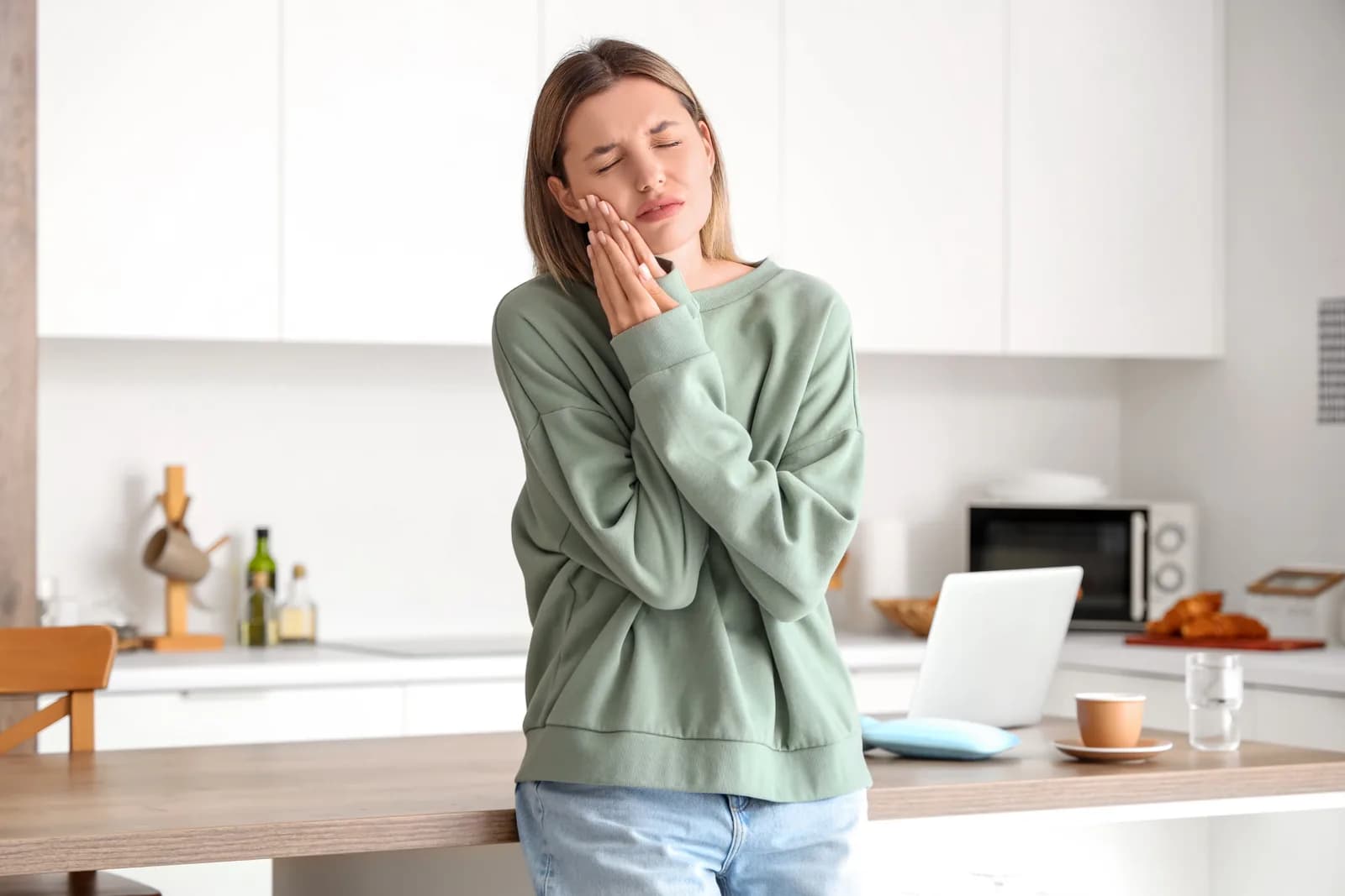 Woman holding her cheek with a toothache, needing urgent dental care