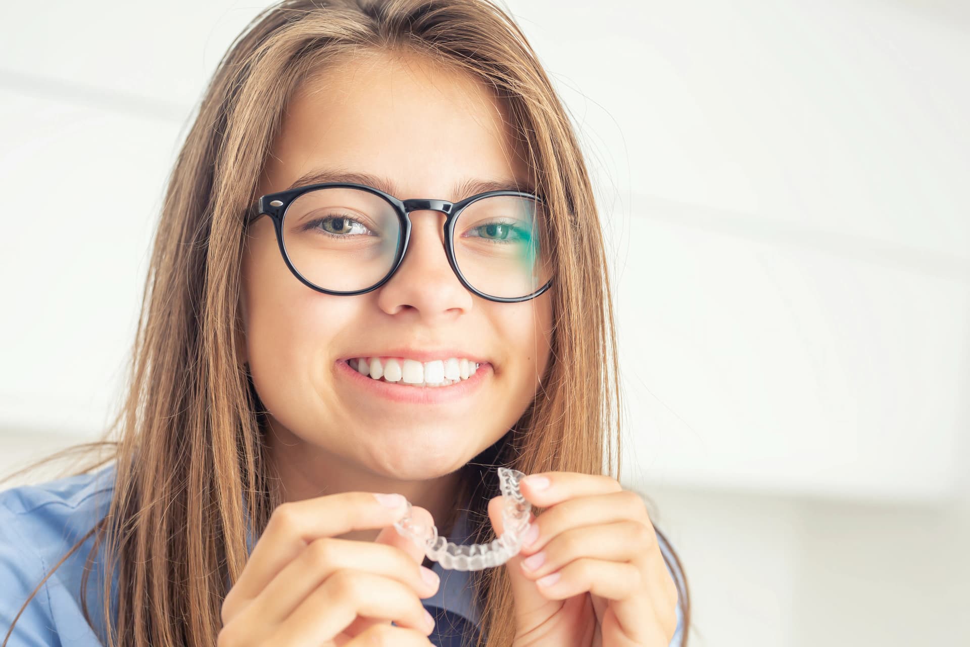 Smiling patient holding a clear Invisalign aligner